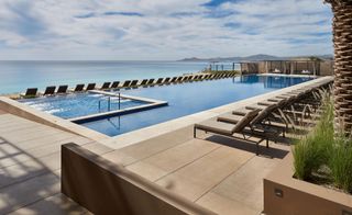 Los Cabos infinity pools with sand colored paving and, beige sun loungers overlooking ocean