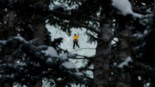 A young man ice climbing, viewed through tree branches, near Telluride, Colorado