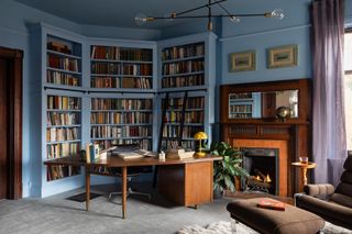 A home library color drenched in blue, with a wooden study table, and modern lights