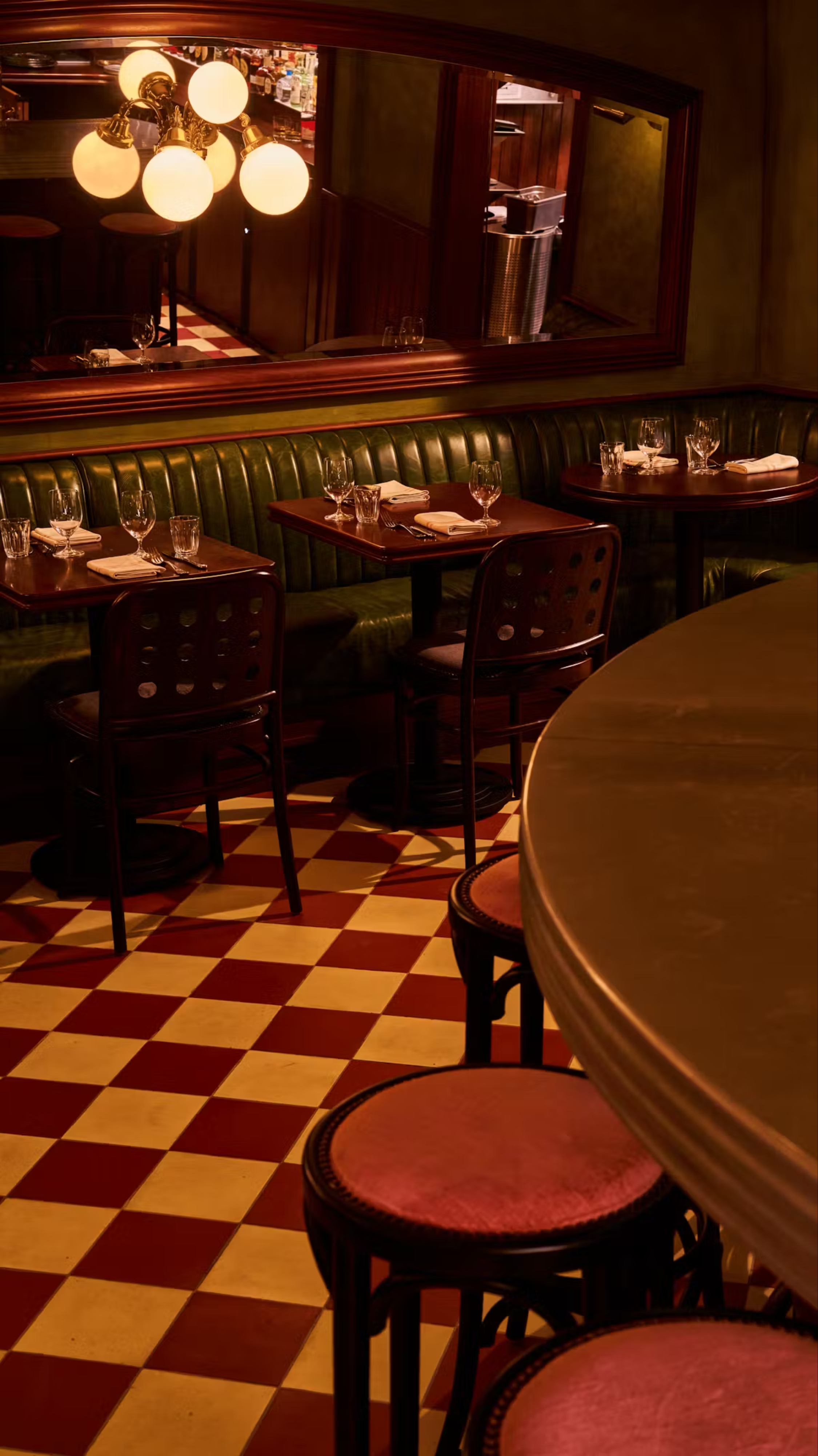the dramatic, members club style interiors of wild cherry restaurant with a checkerboard floor and green leather seats
