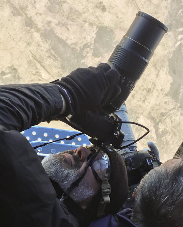 NASA photographer Bill Ingalls hangs out of the door of a helicopter to get a shot.
