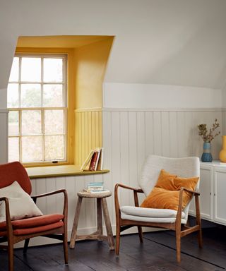 Quiet seating nook with armchairs, white wood paneling, and yellow contrast painted window surround.