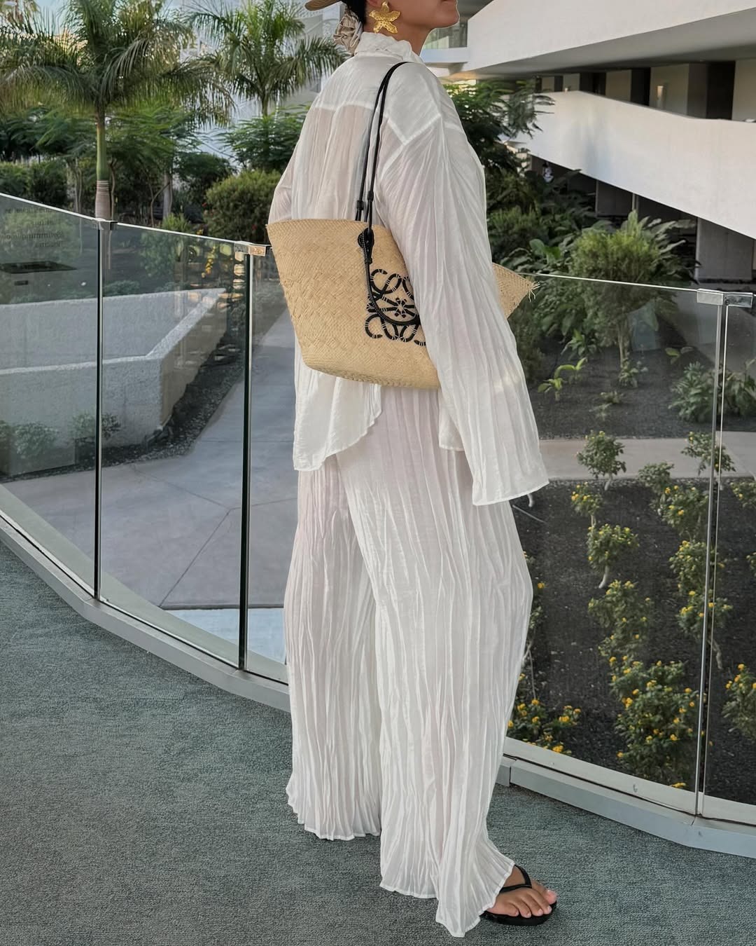Woman wears white shirt, white trousers and woven Loewe basket bag