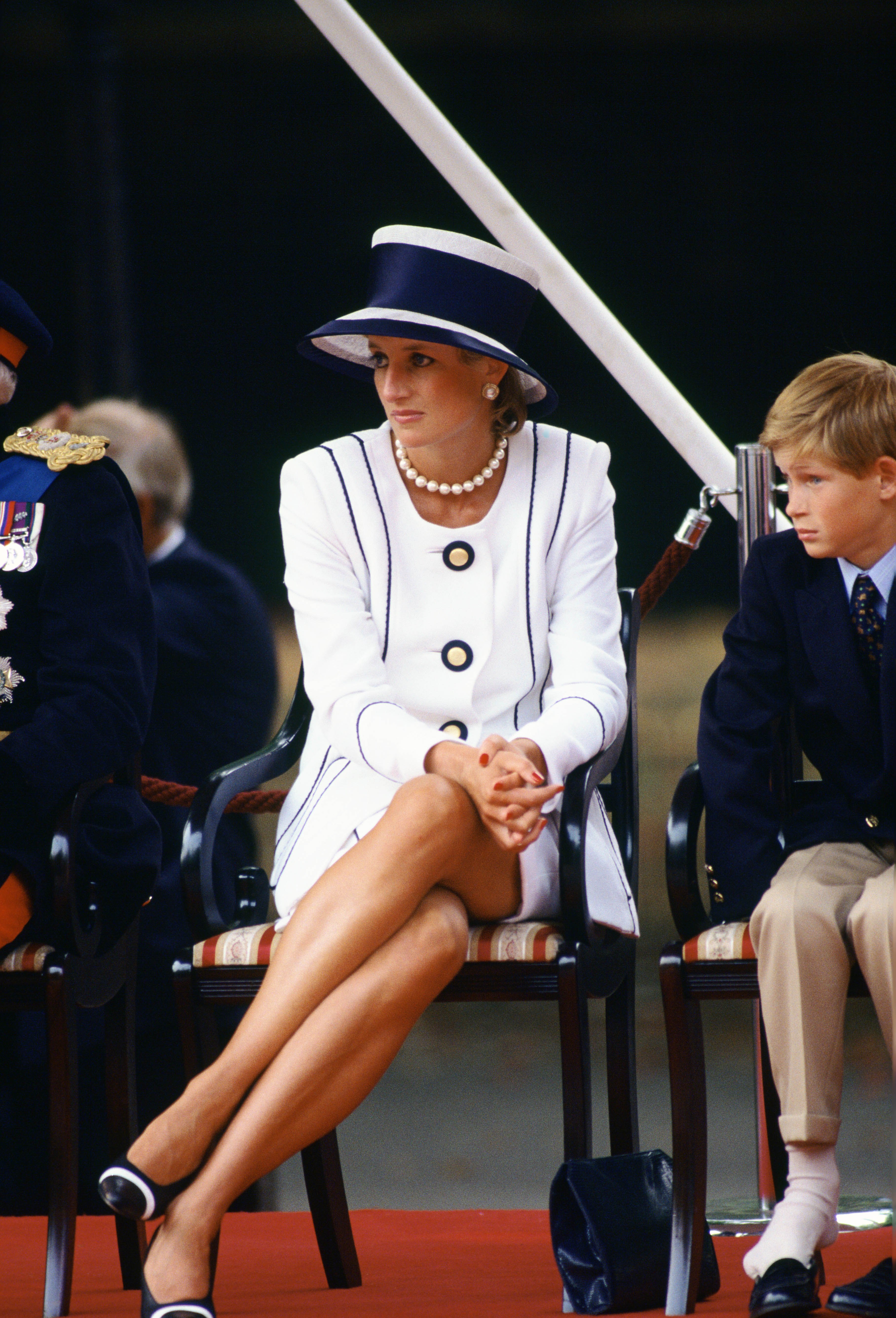 Princess Diana and son Prince Harry attend the VJ Day commemorative events, Diana is wearing a white skirt suit with navy blue trim, a navy hat with white detailing, and matching shoes