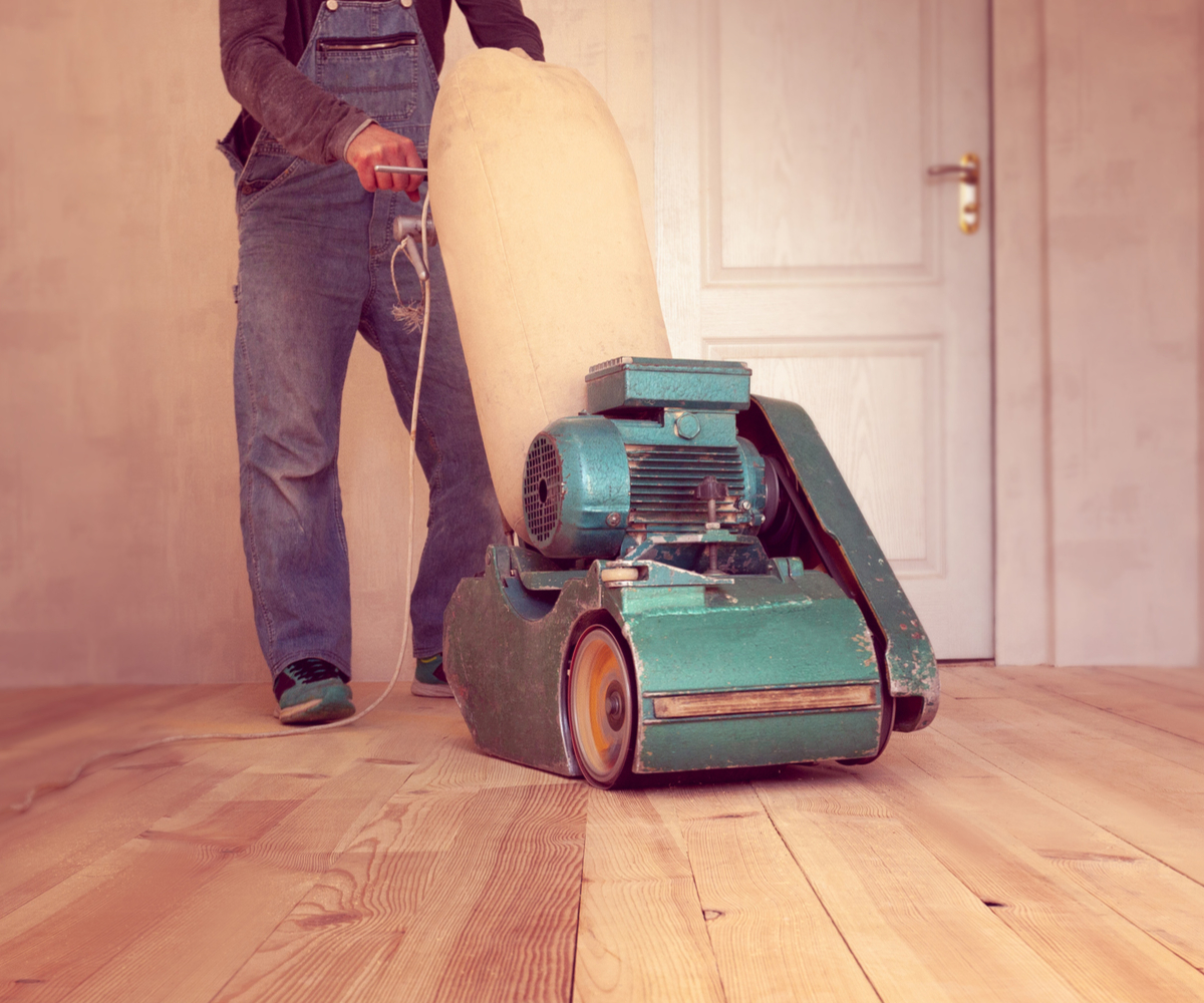 A person pushing a professional-grade floor sander over wooden floorboards