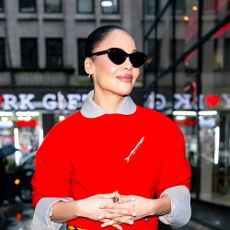 Tessa Thompson wearing a red sweater, brown leather skirt, and beige heels
