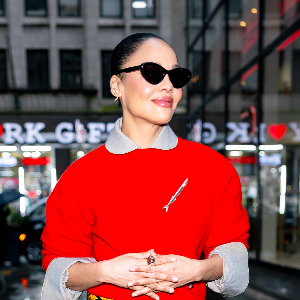 Tessa Thompson wearing a red sweater, brown leather skirt, and beige heels
