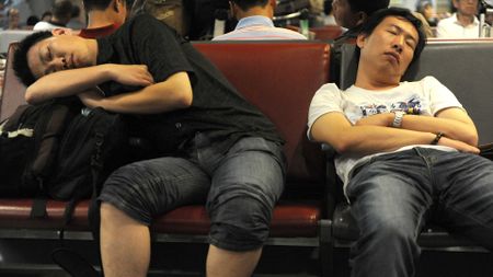 Two men sit with their luggage in an airport.