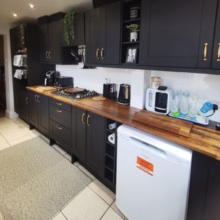black kitchen cabinets with wood worktop and neutral floor tiles