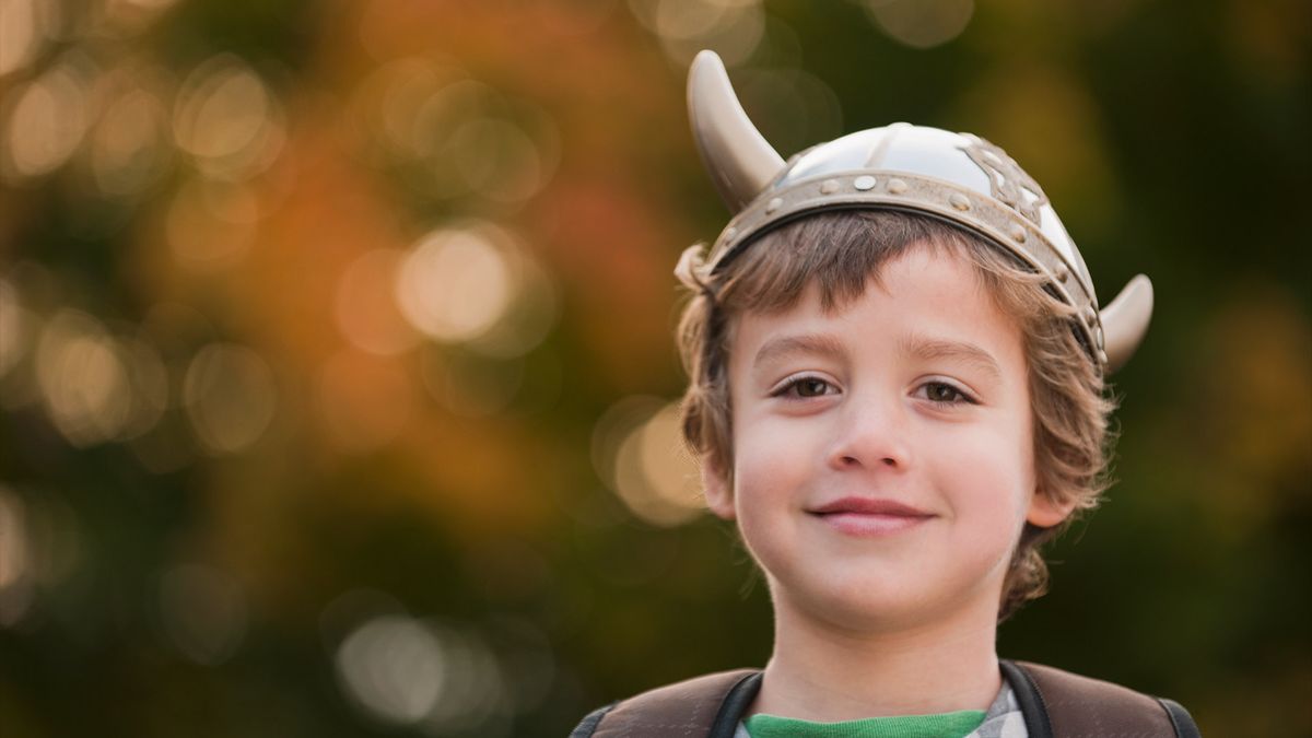 young boy smiles at the camera wearing a plastic viking helmet