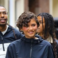 Zendaya wearing a navy and white windbreaker jacket, navy pants, and burgundy sneakers