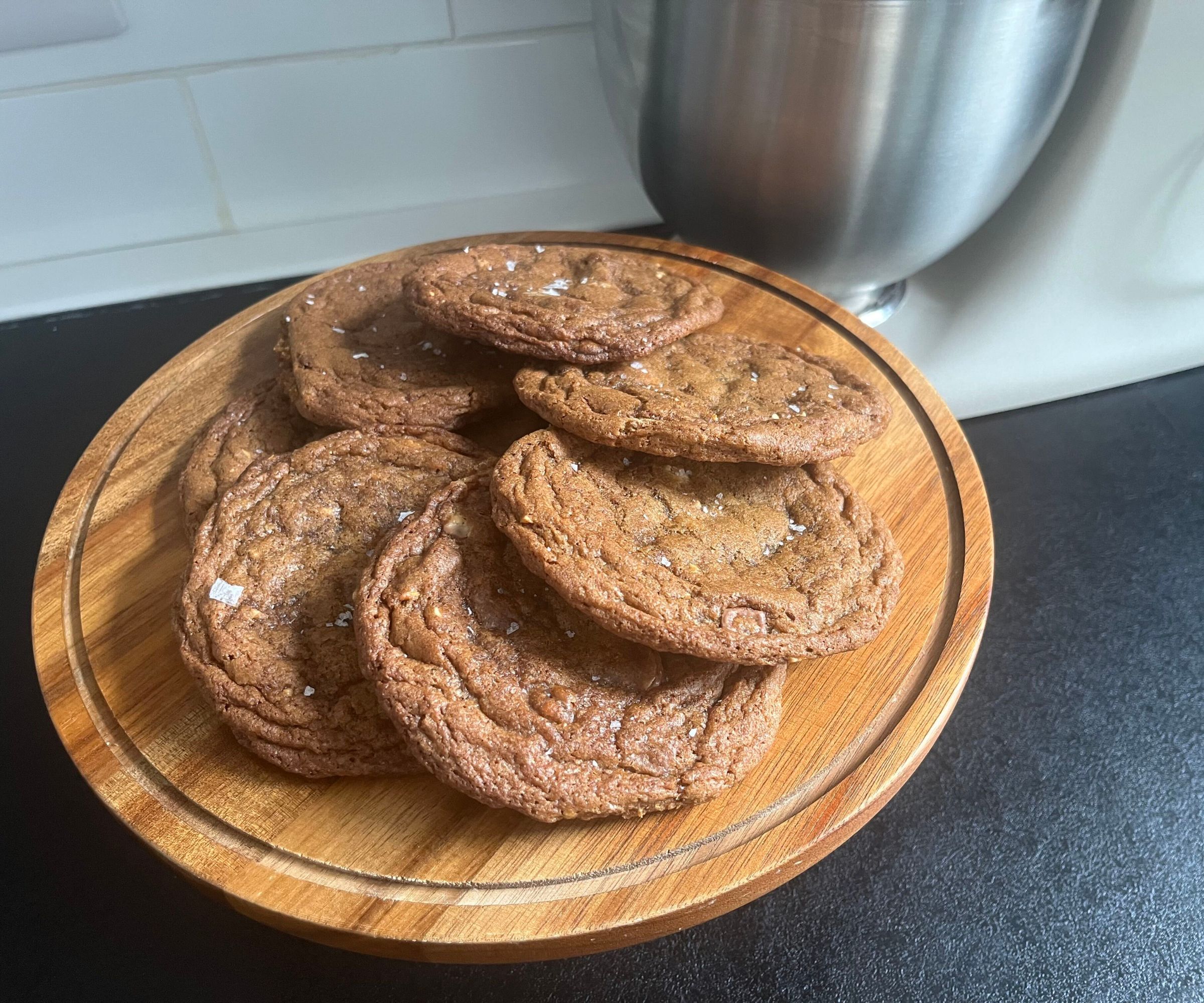 A pile of freshly baked cookies on a cake stand beside a KitchenAid Artisan Plus Stand Mixer