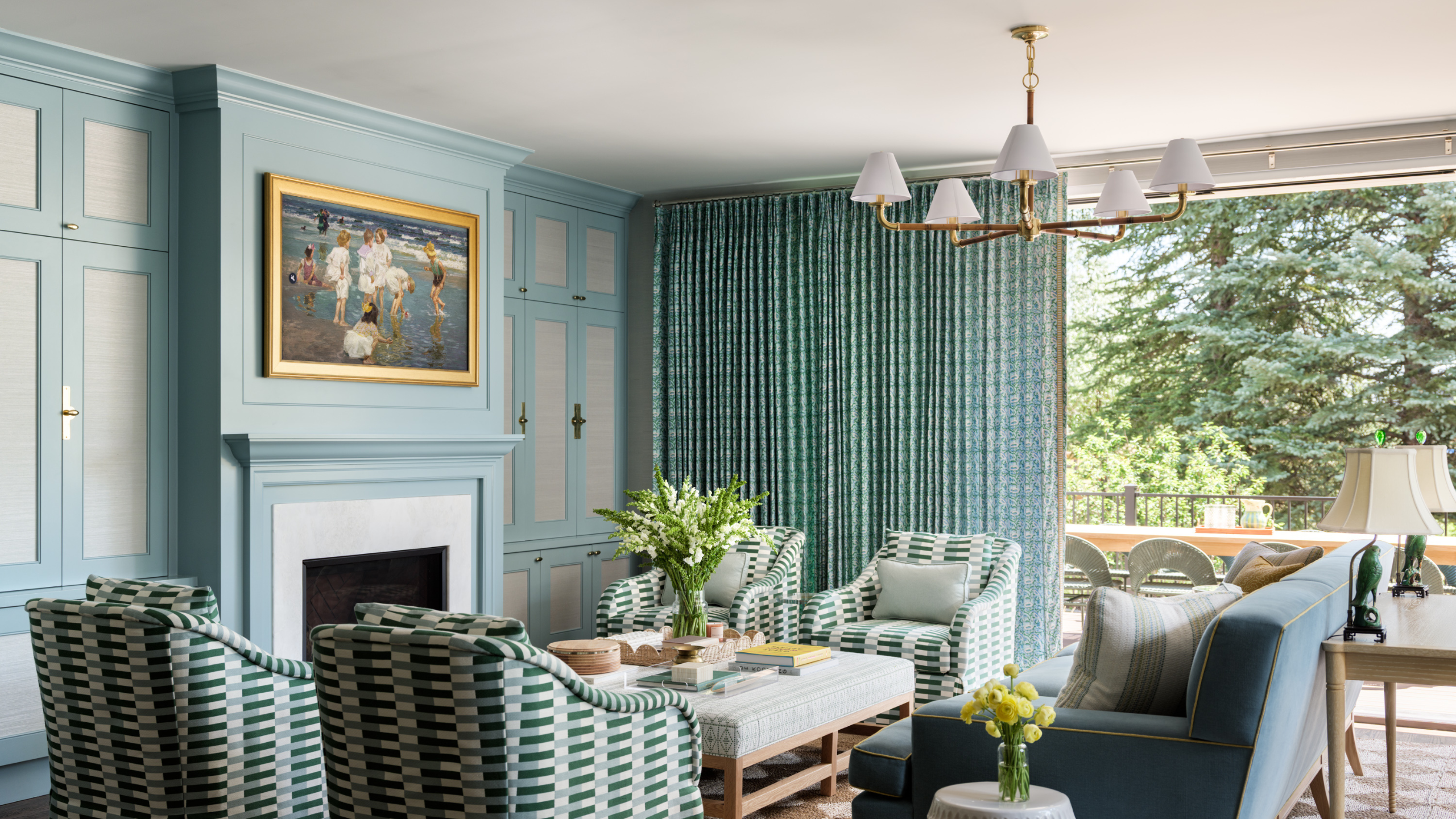 Blue-green Colorado family room with large windows overlooking a lush landscape, painted molding, geometrically patterned club chairs, and a multi-shade chandelier overhead