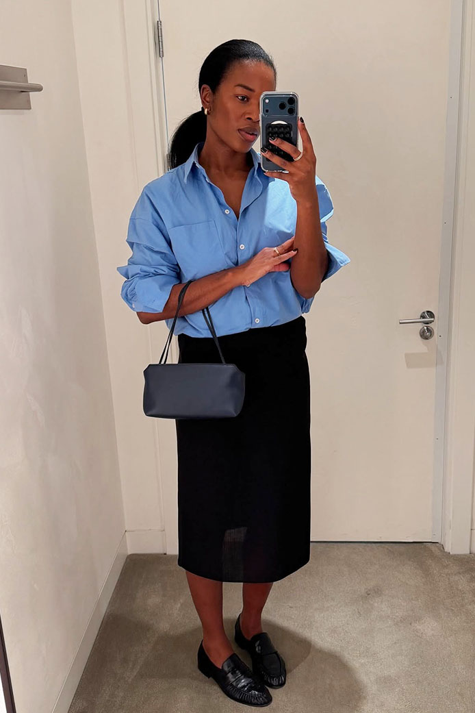 a woman wearing a blue button-down, black skirt, and loafers