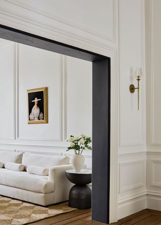 a white living room with paneling, a white sofa, and a checkered jute rug