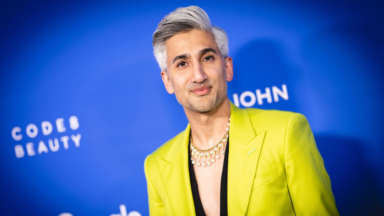 We love Tan France&#039;s guest cottage style which is as stylish as his clothing. Here he is wearing a bright yellow blazer standing against a dark blue background with white lettering