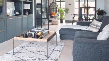 a neutral living room with white panel walls, white couch with yellow cushions and blue striped throw and a distressed black wood chest of drawers