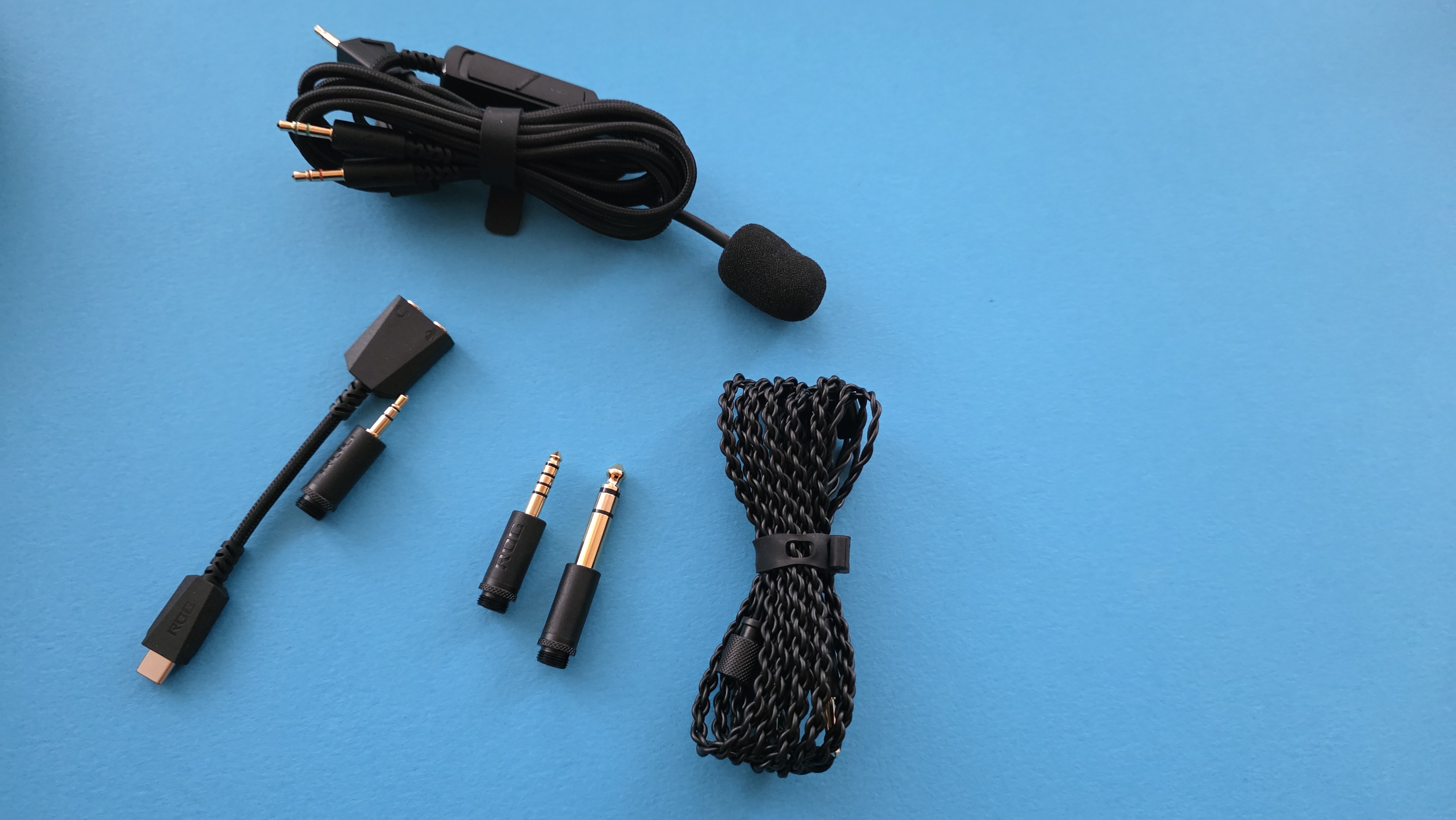 Coiled black cables and a small microphone arranged on a blue background. Two gold-plated audio adapters are in the center.