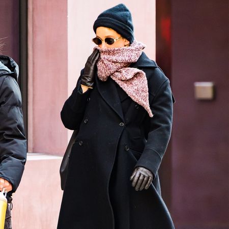 Jennifer Lawrence wears a black beanie, sunglasses, red scarf, black jacket, black Loewe sneakers, and red socks.