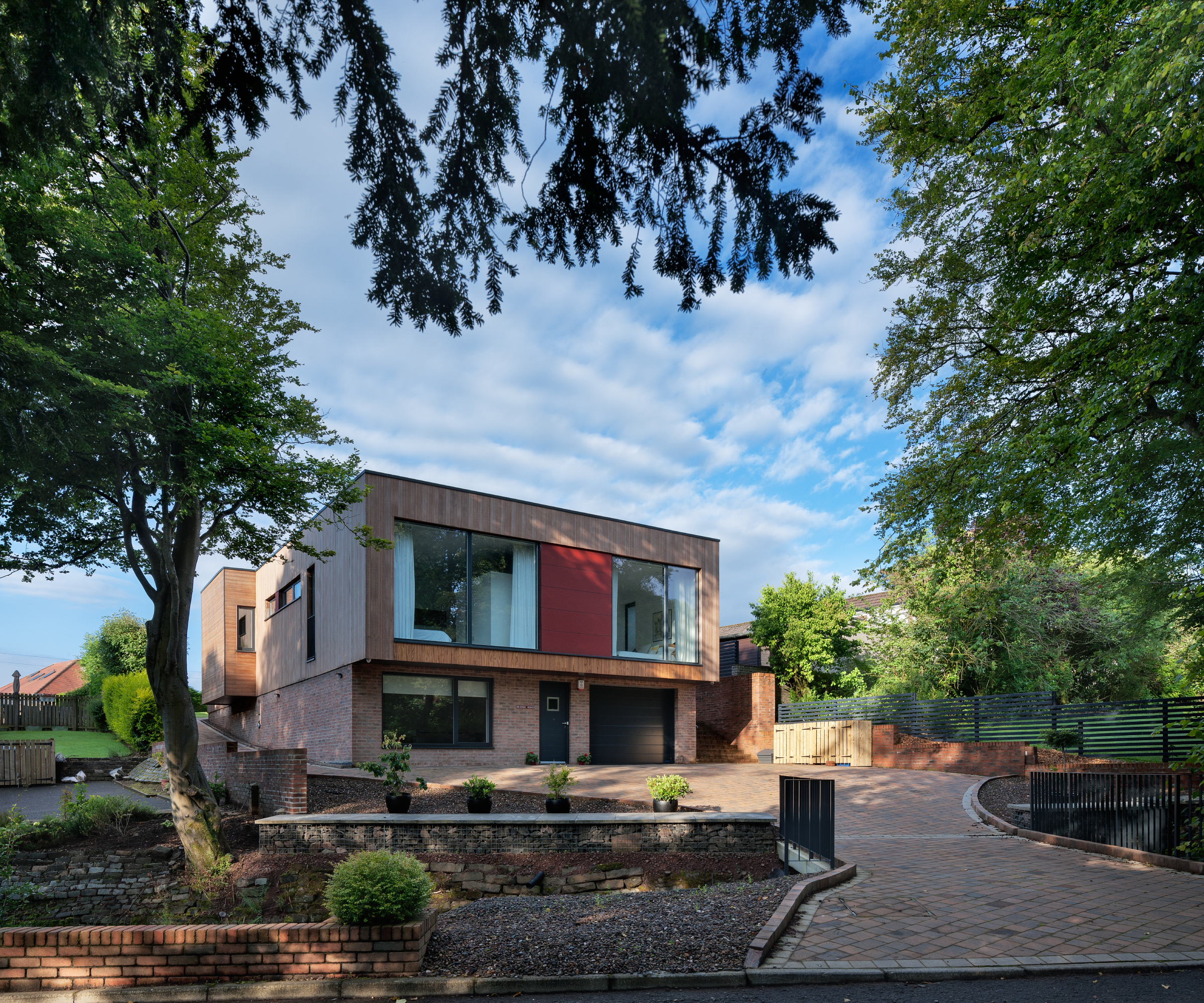 modern self build house with large picture windows and a sloping block paved driveway leading to house