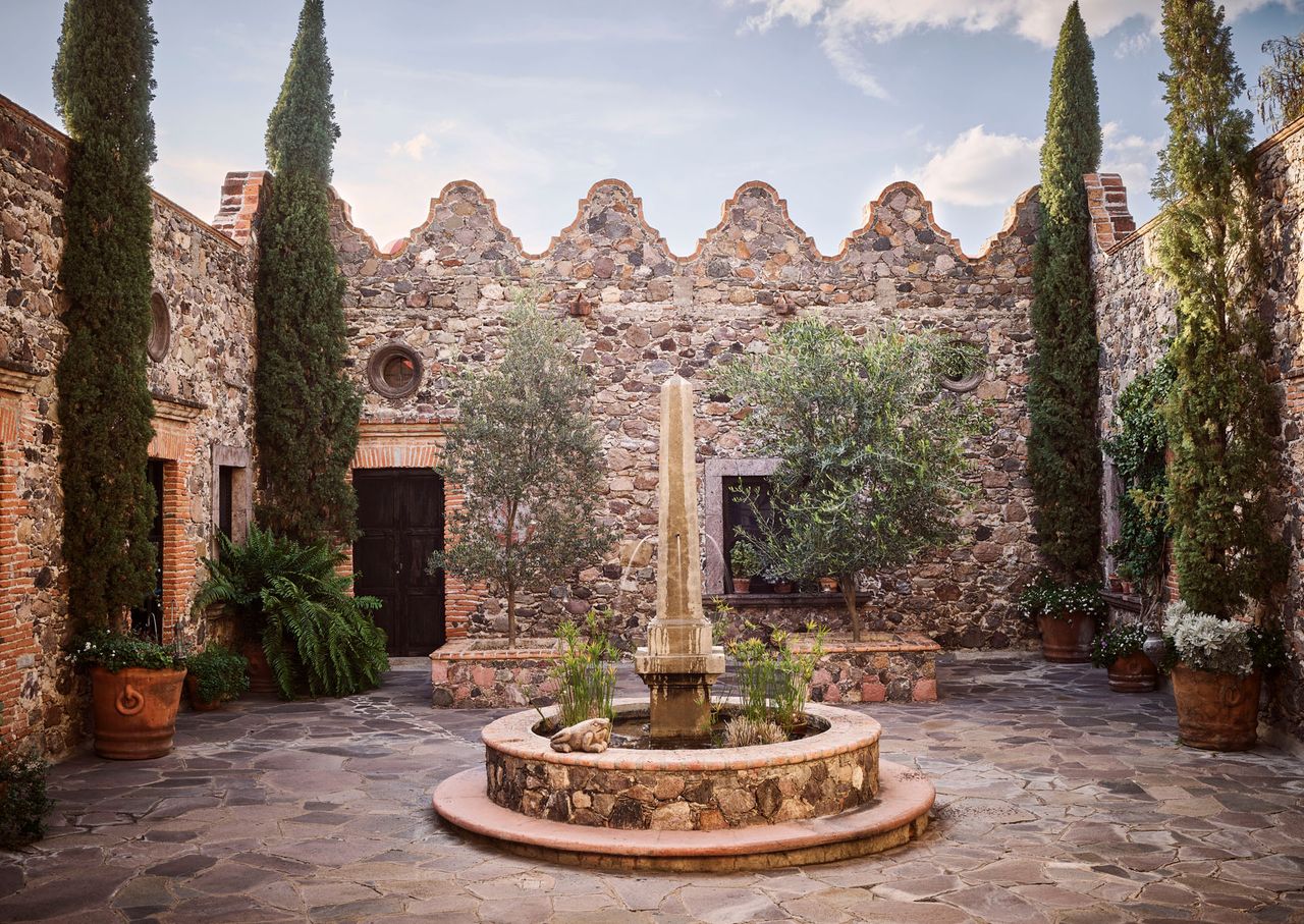 Outdoor area with stone floor, stone fountain, stone walls and trees