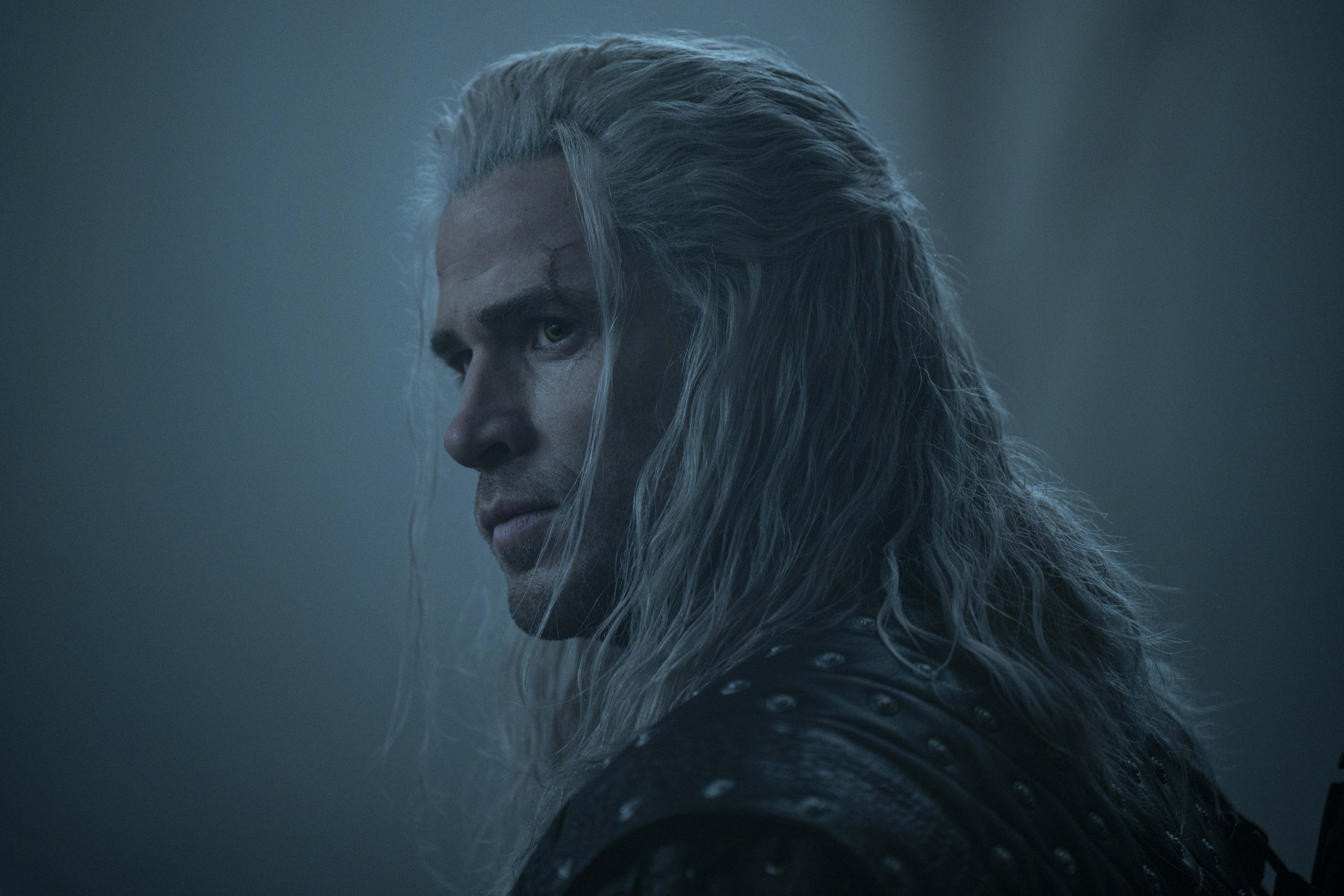 liam hemsworth as geralt looking over his shoulder in a dimly lit wood in the witcher season 4