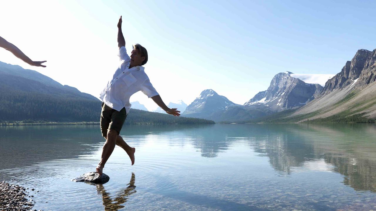 A man losing his balance while standing on a stone in a pond