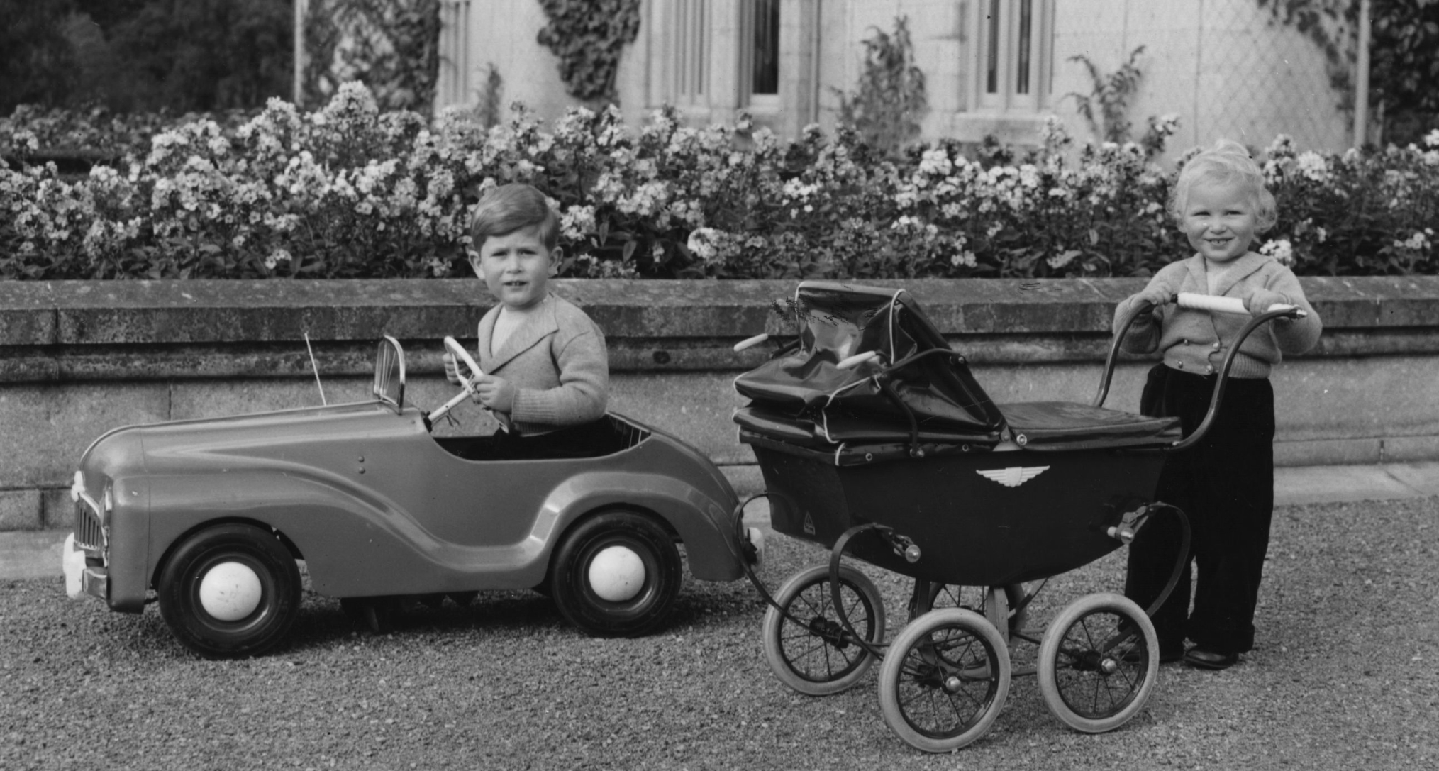 King Charles and Princess Anne playing with a toy car and buggy as kids