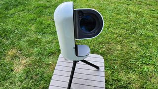 The Vaonis Vespera Pro smart telescope pointing at the sky on a brown table with grass in the background.