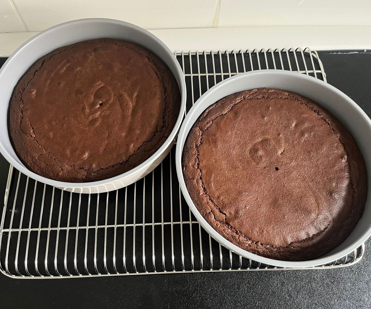 Two grey cake tins with chocolate cake inside on a wire cooking rack