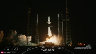 A white and black rocket fires its engines while lauching from a pad at night