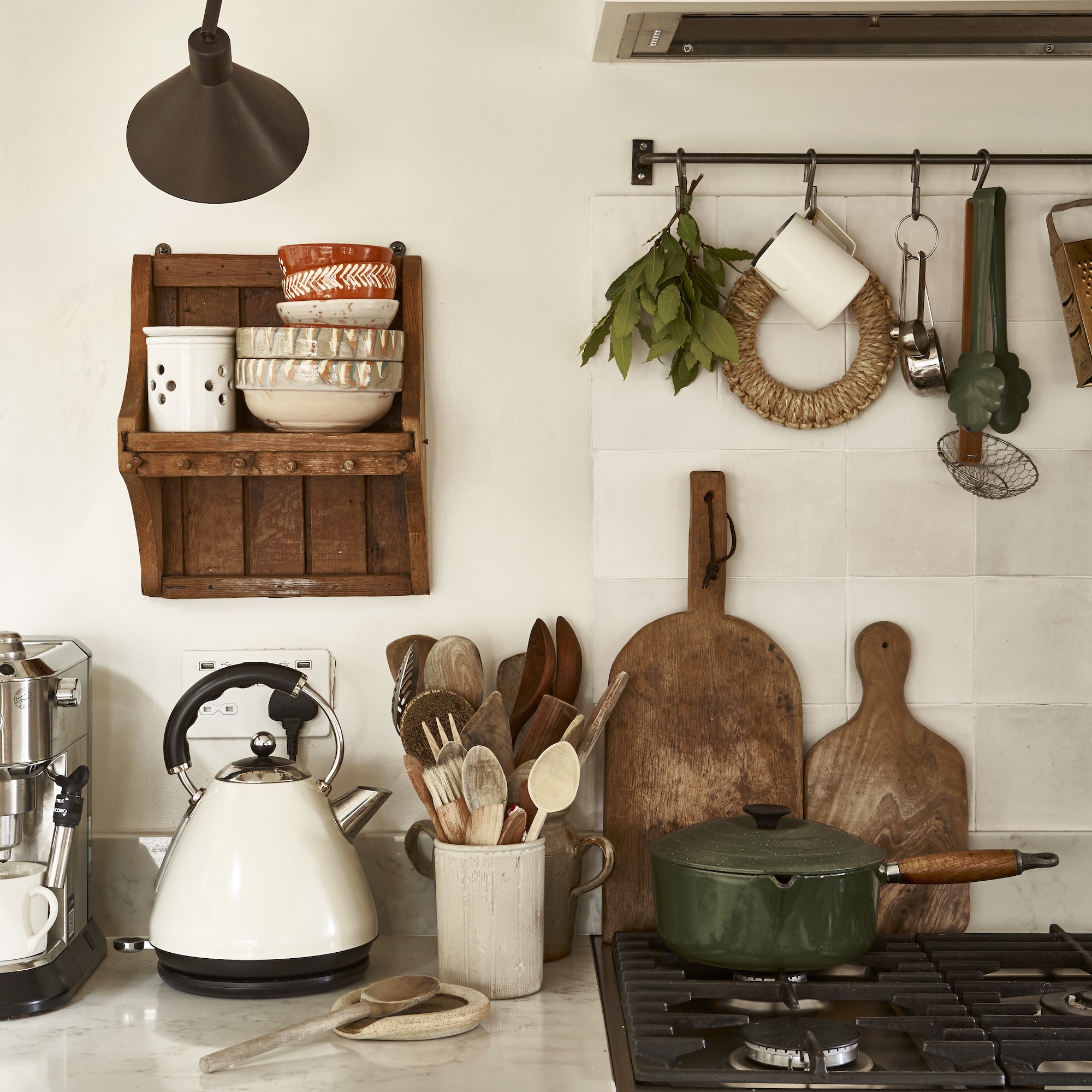 kitchen with gas hob and hanging utensil rail above, with workstop with wooden spoons and cream kettle