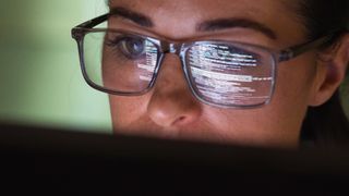 Software developer coding in VBScript programming language at a computer with screen reflecting in glasses.