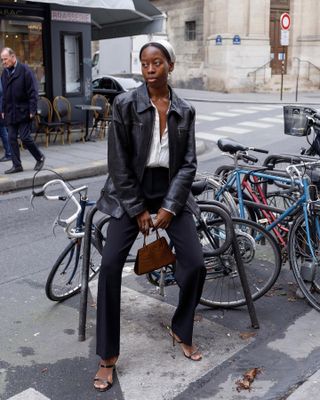 French fashion influencer Syvlie Mus is Paris wearing an on-trend fall look including a vintage leather jacket, head scarf, white shirt, black pants, strappy heels, and a mock croc bag.