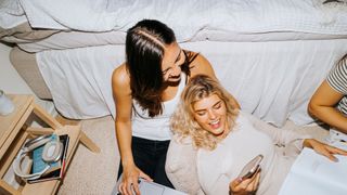 Two female students sitting on the floor of a dorm room at college.