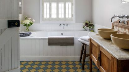 An example of white bathroom ideas showing a white bathroom with a built in bath below a window and colorful floor tiles