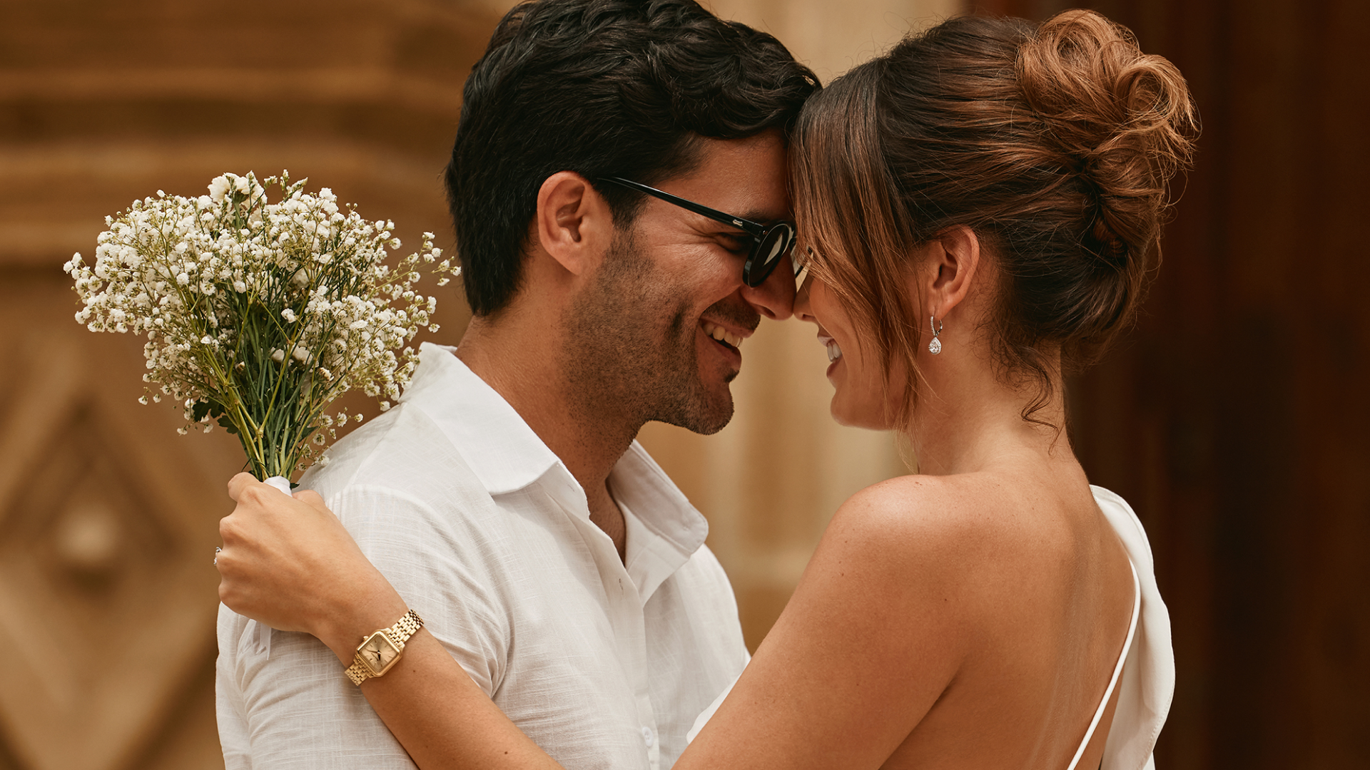 A couple on their wedding day featuring a woman wearing a gold Bulova watch and holding a bouquet of white flowers
