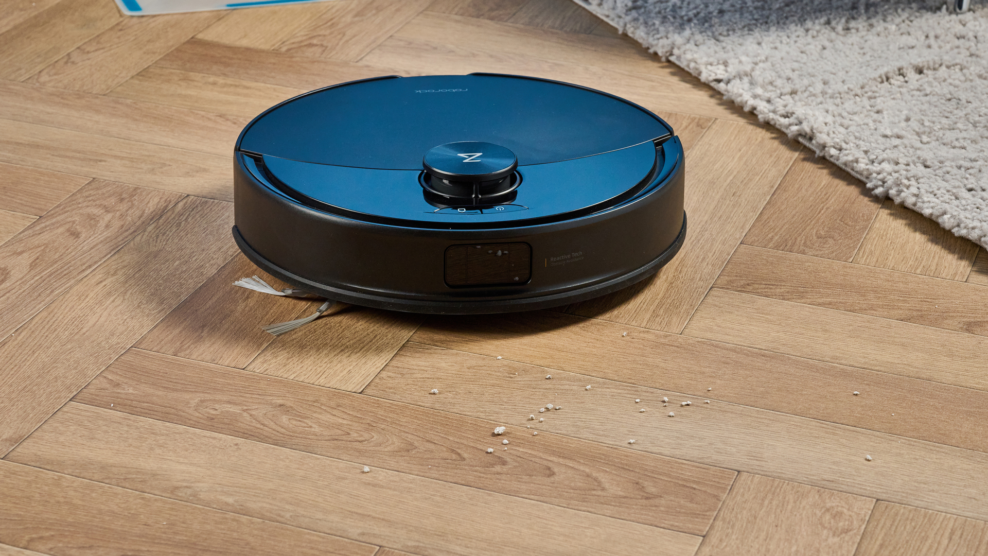 Roborock Q10 S5+ photographed on a wooden floor in front of a blue background