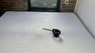 A black weight is placed next to a tape measure and a wine glass during our Layla Essential Mattress review motion isolation test