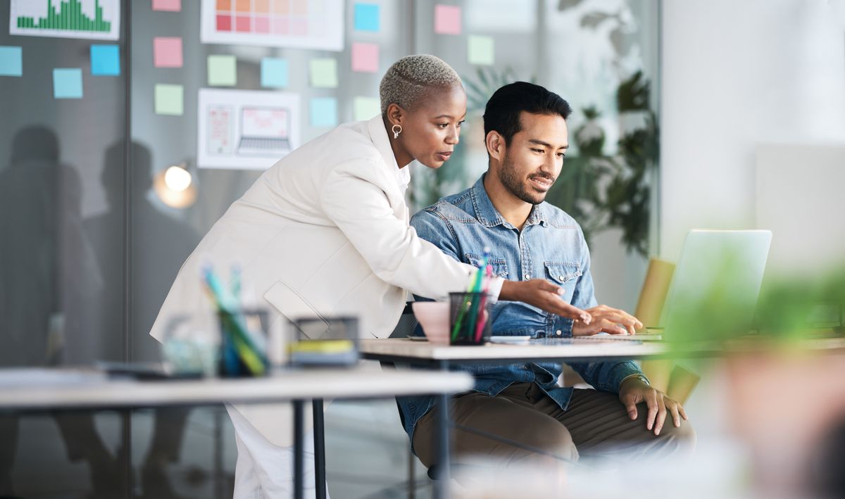 A business woman looking over a colleague&#039;s shoulder at some work he is doing and offering advice