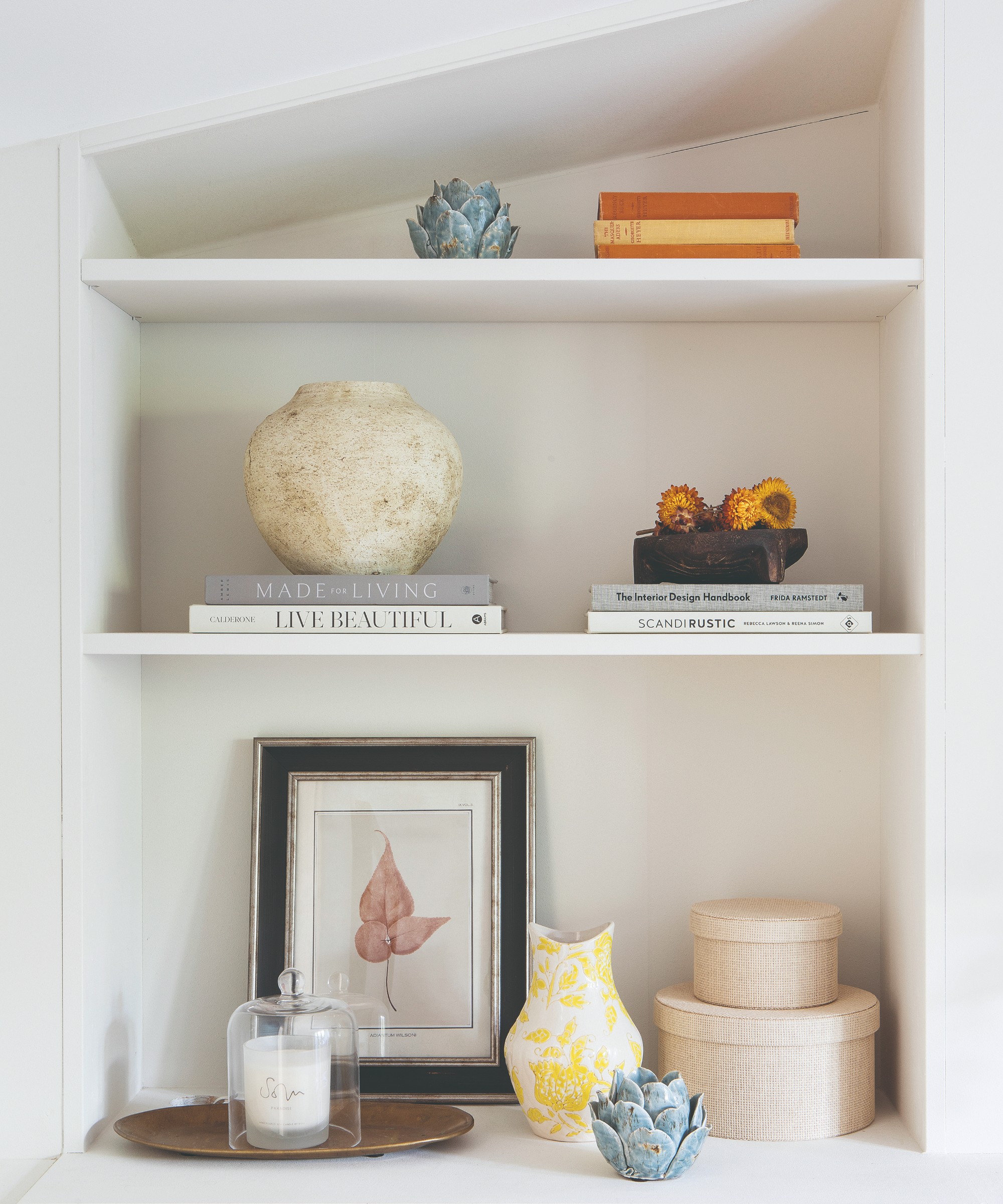 Built-in shelves painted white styled with books, decorative objects and a scented candle