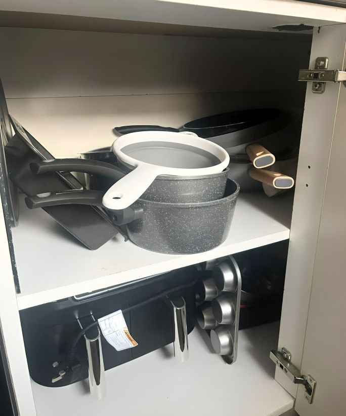 Gray pots and pans haphazardly scattered across a cabinet shelf
