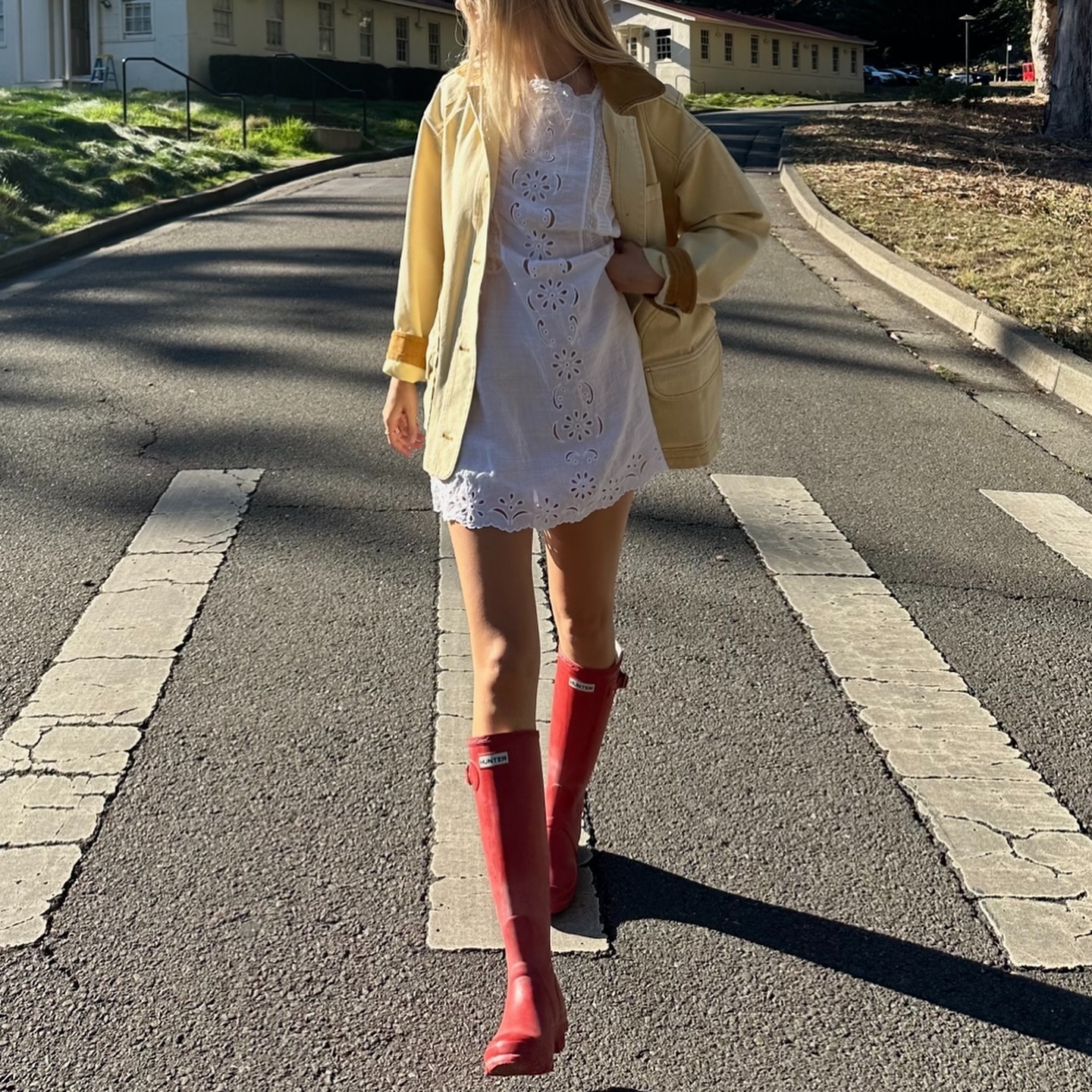An image of @caitlinburnhamm  wearing a country jacket from Dôen with a white lace mini dress and red gumboots.