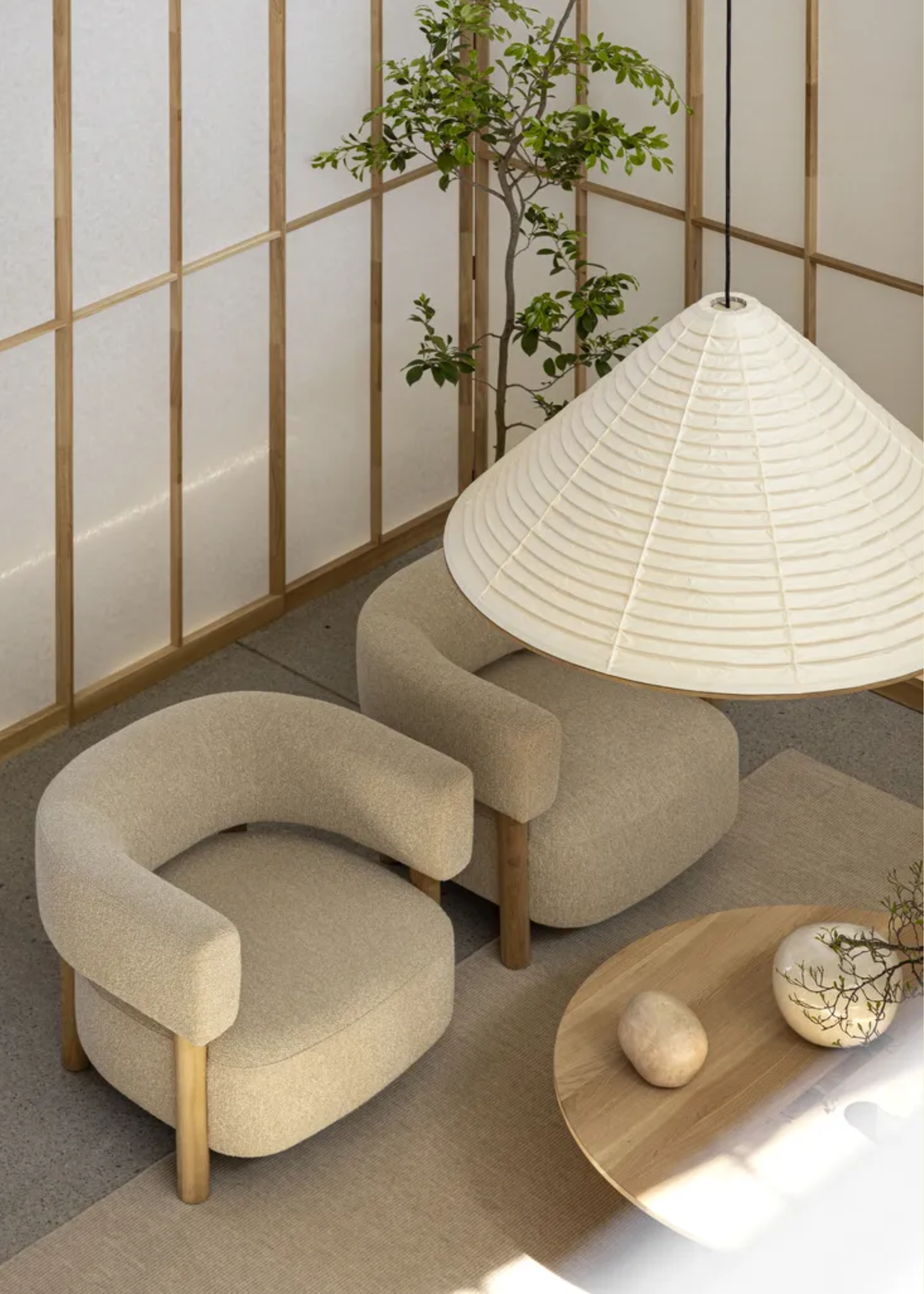 A living room with a paper lantern pendant, rice paper walls, a pair of beige armchairs, a potted tree, and a round coffee table with vases