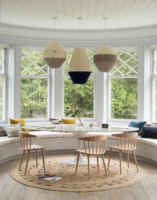 Dining room built into a curved window with neutral colors and pendant lights