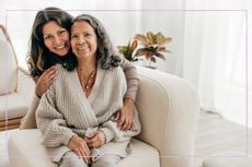 Mother smiling on the sofa with daughter standing behind hugging her