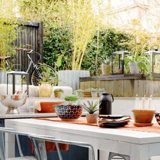 outdoor living area with fun patterned paving, white wooden table with metal chairs and raised level above