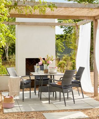 An outdoor living area with an outdoor fireplace, a wooden pergola, and a black outdoor furniture set with four chairs and a square table