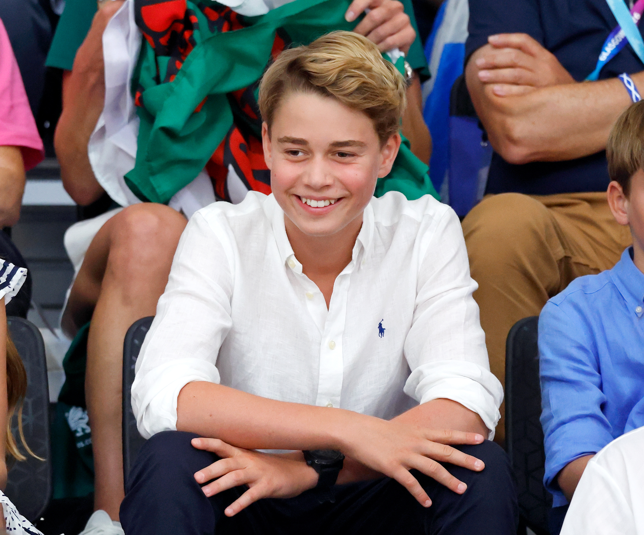Prince George wearing a white shirt and smiling sitting in the stands at Commonwealth Games