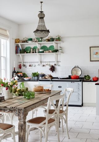 a white kitchen with open shelves and blue aga, and a wooden dining table